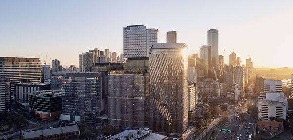 The towers of Collins Square extending high into the sky as the distant setting sun reflects off their glass façades.