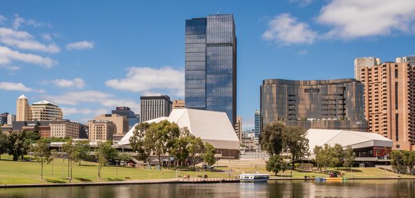 The tall Festival Tower building extending high above the buildings of Festival Plaza in Adelaide. The neighbouring grassy parklands and calm waterway surround the precinct.