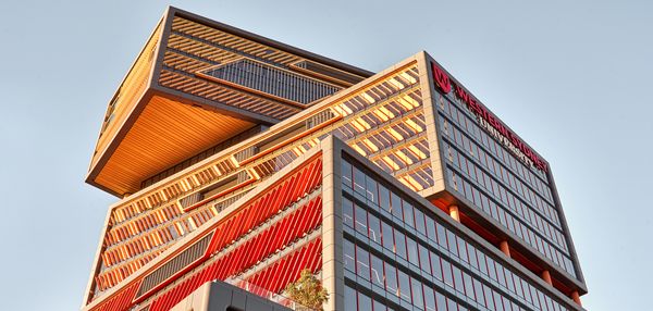 The main Western Sydney University building seen from below, with its unique rotated stacked sections shining orange in the sunlight.